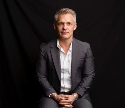 Portrait of a male biotech executive sitting in front of a black background looking confidently looking into the camera lens.