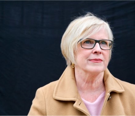 Natural portrait of a middle-aged female cancer patient looking thoughtfully off-camera in front of a black backdrop.