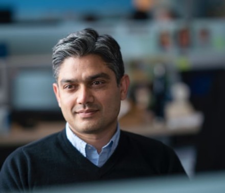 Naturally lit lifestyle portrait of a male biotech employee thoughtfully looking off-camera at his workstation.