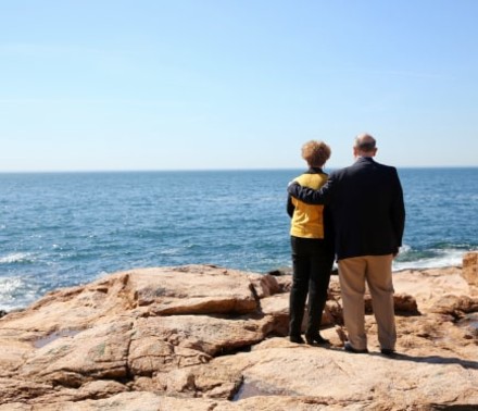 Environmental portrait of a cancer patient holding the shoulder of his wife as they look out at the ocean.
