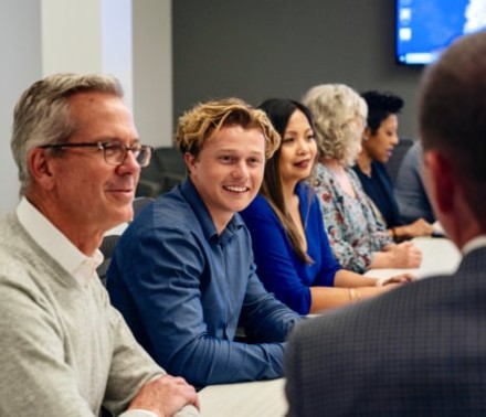 Group portrait of a biotech team made up of various aged men and women all smiling or engaged in conversation.