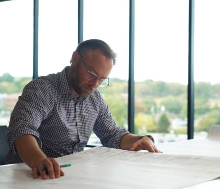 Lifestyle portrait of an architectural engineer looking intently at blueprints in his naturally lit office.