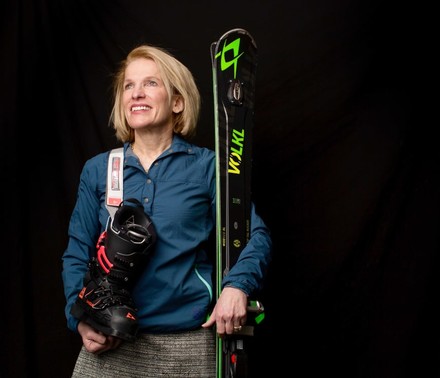 Lifestyle Portrait of a middle-aged female biotech CEO dressed professionally while holding snow skis and boots for a profile on executive hobbies.